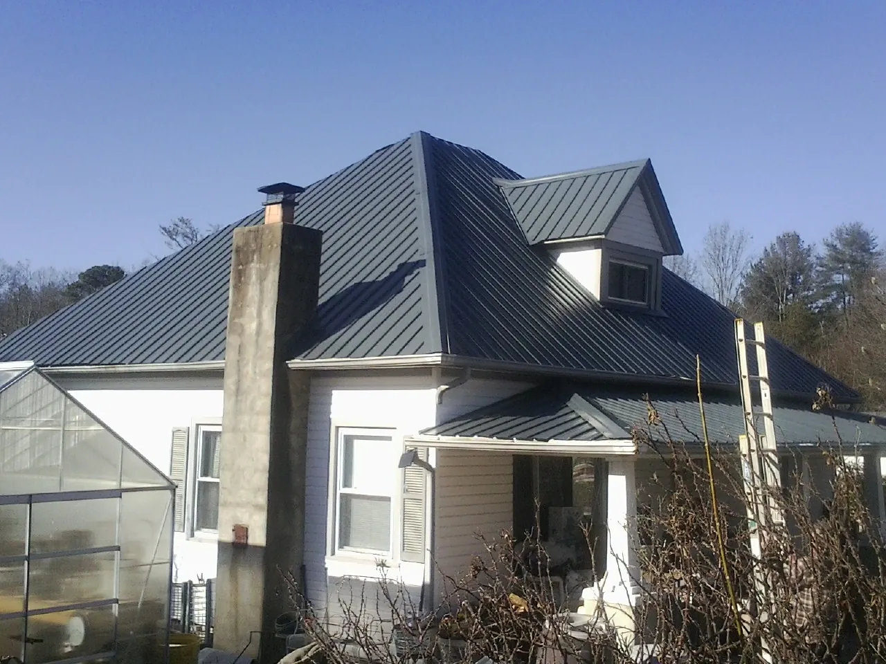Dark blue standing seam metal roof on a white farmhouse with dormer — Slate & Tile Roof Repair by Roofing Brothers in Indian Springs