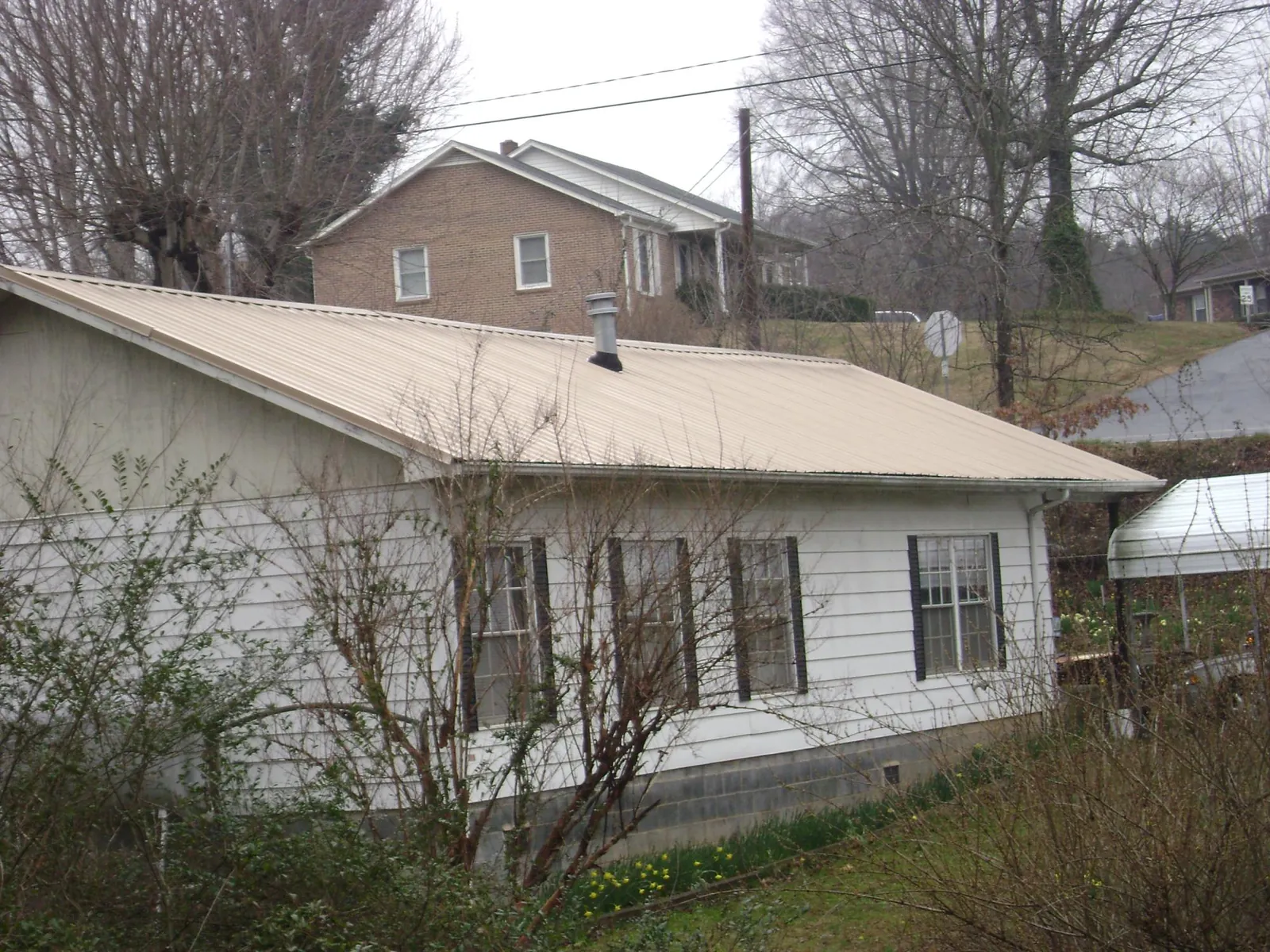 Tan metal roof on a white sided house set into a hillside — Commercial Roofing by Roofing Brothers in Indian Springs